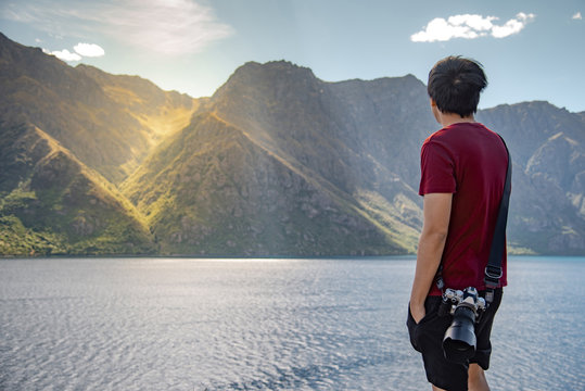 Young Asian man photographer looking at mountain and lake scenery in South island of New Zealand. Travel and landscape photography concepts