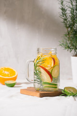 Detox water with lime, organe, apple and rosemary in a mason jar glass with a white wooden background