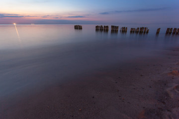 smooth sea surface and breakwaters in purple twilight on long exposure