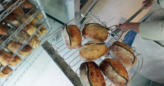 Baker pulling breads from oven and putting on shelves stacked