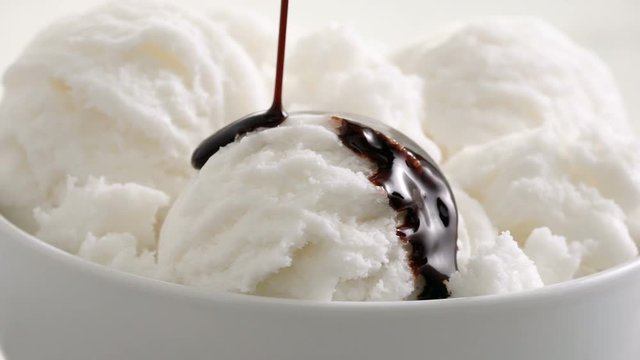 Vanilla ice cream with slow motion chocolate syrup being poured over the bowl. 