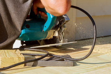 handsome man carpenter using a circular saw installing a wood floor outdoor terrace in new house