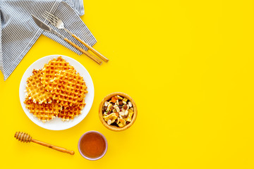 Hot round waffles ready to eat. Belgian recipe. Waffles on plate near honey and dried fruits on yellow background top view copy space