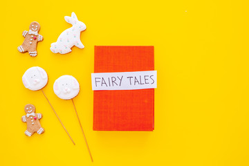 Fairy tales book near gingerbread man and candies on yellow background top view space for text