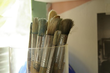 glass jar of well used varying artist's paint brushes drying in the artist's studio