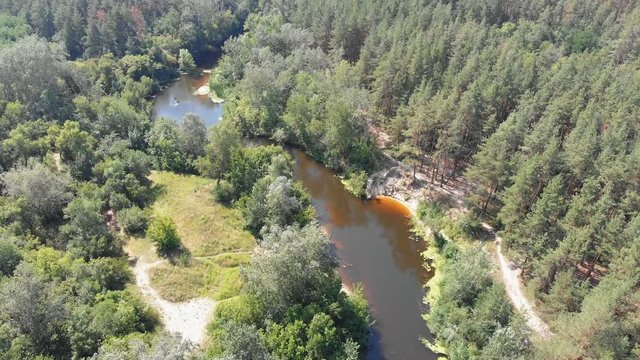 The river bed is a top view from the drone. The quadrocopter is flying over the river in the forest. Summer, sunny day.