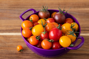 Freshly picked heirloom tomatoes, yellow, red, and purple, in a purple plastic colander on a wood cutting board

