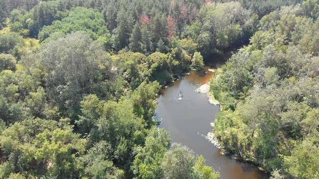 The river bed is a top view from the drone. The quadrocopter is flying over the river in the forest. Summer, sunny day.