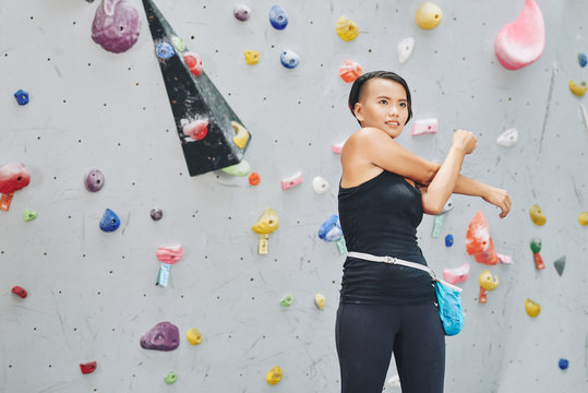 Pretty Vietnamese woman warming-up before bouldering on artificial wall
