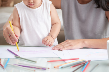 Cropped image of little girl drawing with pencil under control of her mother