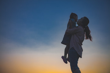 Silhouette of a happy little girl child running into the arms of his loving mother for a hug.