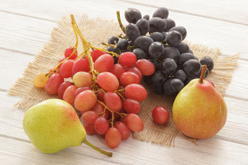 Fresh sweet grapes and pear on burlap napkin on wooden table closeup