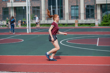 Obraz premium Red-haired young girl runs in the stadium. Student delivers standards for running outdoors. Young woman running on the football field