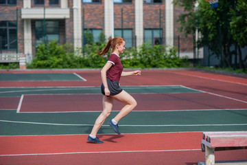 Obraz premium Red-haired young girl runs in the stadium. Student delivers standards for running outdoors. Young woman running on the football field