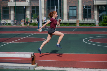 Obraz premium Red-haired young girl runs in the stadium. Student delivers standards for running outdoors. Young woman running on the football field