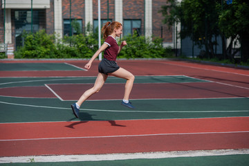 Red-haired young girl runs in the stadium. Student delivers standards for running outdoors. Young...