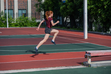 Red-haired young girl runs in the stadium. Student delivers standards for running outdoors. Young woman running on the football field