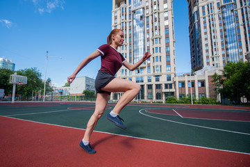 Red-haired young girl runs in the stadium. Student delivers standards for running outdoors. Young...