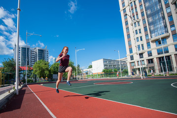 Obraz premium Red-haired young girl runs in the stadium. Student delivers standards for running outdoors. Young woman running on the football field