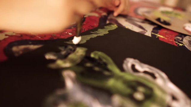 Young girl painting alone in dimly lit room on colorful table shot in close up and and artistic way using slow motion