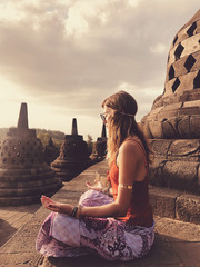 Young woman practicing yoga - meditation on the biggest Buddhist temple - Borobudur. - obrazy, fototapety, plakaty
