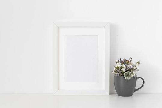 Minimal white A5 portrait frame mockup with small bouquet of dried flowers in gray mug on white wall background. Empty frame, poster mock up for presentation design. Template frame for text, lettering