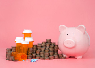 Pink piggy bank next to stacks of coin cash piled high around Rx prescription drugs, pills spilled...