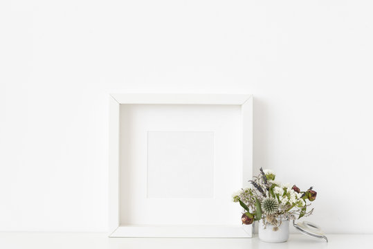 White square portrait frame mockup with small bouquet of dried flowers in small white pot on white wall background. Empty frame, poster mock up for presentation design. Template frame for text
