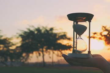 Young woman holding Hourglass during sunset. vintage style.