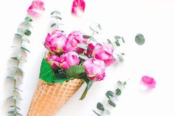 Creative flowers composition with waffle cone with pink roses and eucaliptus inside on white background. The concept of gift and celebration. Flat lay, top view.