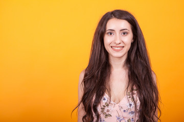 Fototapeta premium Attractive young woman smilling at the camera in studio over yellow background in short dress.