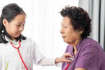 Asian child playing doctor at home, girl doctor checking up her grandmother.