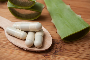 closeup of sliced aloe vera leaves and pills in spoon on wooden background