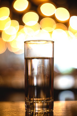 Drinking water, sparkling soda in clear crystal glass on glossy shine table with light flares and bokeh background