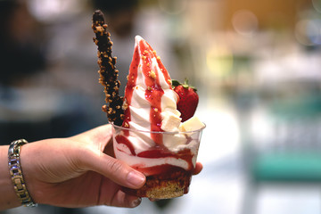 Woman hand holding Gelato ice cream with strawberry sauce and chocolate stick for party time in Summer