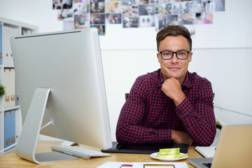 Portrait of cheerful web designer sitting at office table with apple slices on plate in front of him