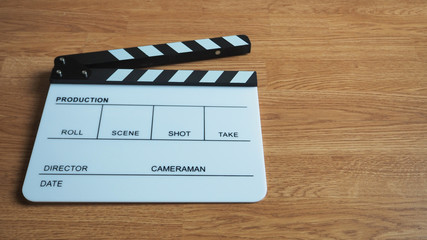 Clapperboard or clap board or movie slate use in video production , movie, cinema industry . It's white color on wood background.