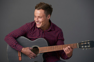 Obraz premium Happy young man in plaid shirt playing acoustic guitar