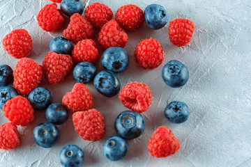 Blueberries and raspberries mix on the background of gray cement. Ripe and juicy fresh raspberries and blueberries close-up. A lot of berries close-up.