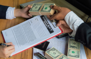 Businessmen use money to bribe other people in exchange for signing contracts, with blurred soft background to Dark business concept