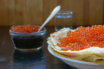 traditional thin Russian pancakes with red caviar on a dark rustic wooden background