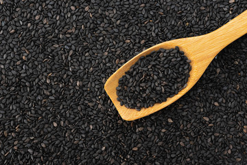 Black sesame seeds on wooden spoon background texture pattern