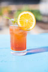Glass of aperol spritz with mint and a orange slice on a sunny day.