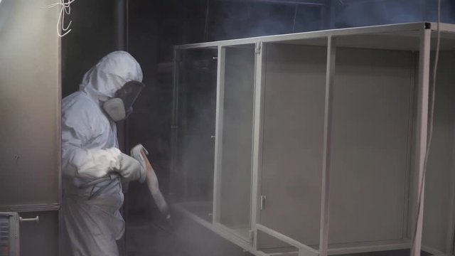 Man painting with spray paint gun in workshop. Clip. Industrial metal coating. Man in protective suit, wearing a gas. Professional factory worker paints metal with guns at manufacture automatic powder