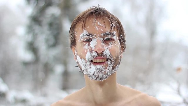 man with a beard, washes his face with snow in winter and smiling, face closeup