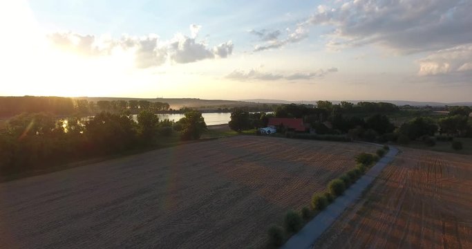 Luftaufnahme - leichter Aufstieg mit Blick über Feld in Richtung Fluß beim Sonnenuntergang