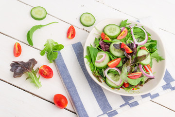 Vegetable salad with fresh lettuce, tomatoes and cucumber in white plate on white table