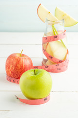 Green and red apples in soda bottle with measuring tape on white table