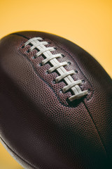 close up of brown american football ball isolated on yellow