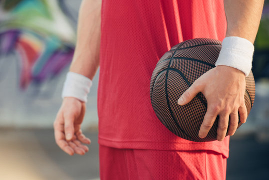 cropped image of basketball player in red sportswear holding basketball ball on street